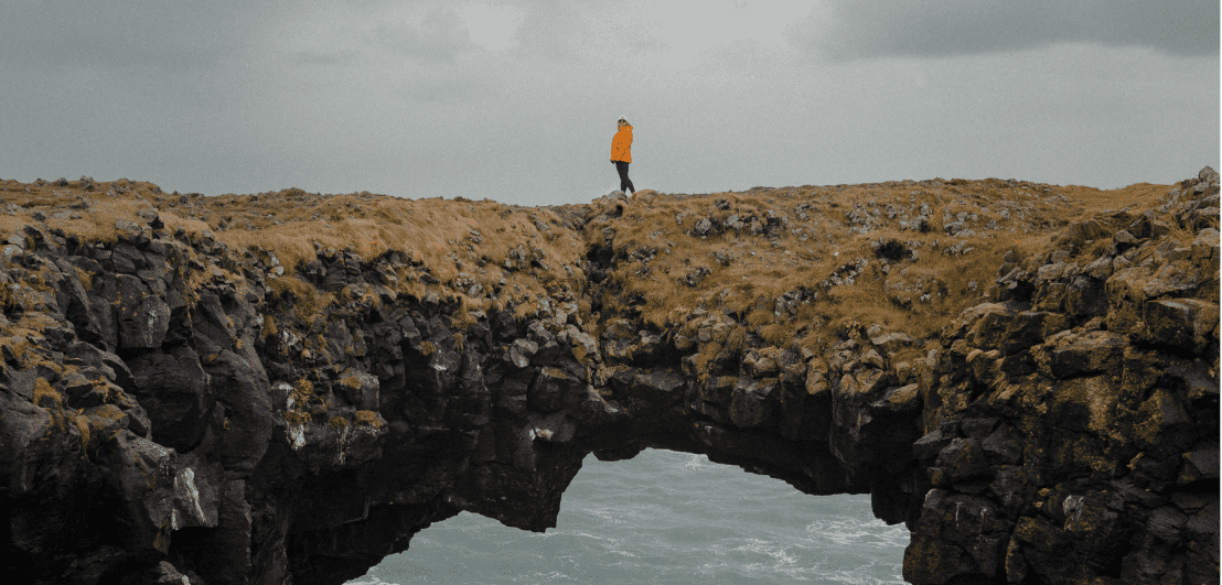 a woman in an orange rainjacket wandering on cliffs near the ocean in rainy weather