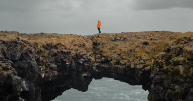 a woman in an orange rainjacket wandering on cliffs near the ocean in rainy weather