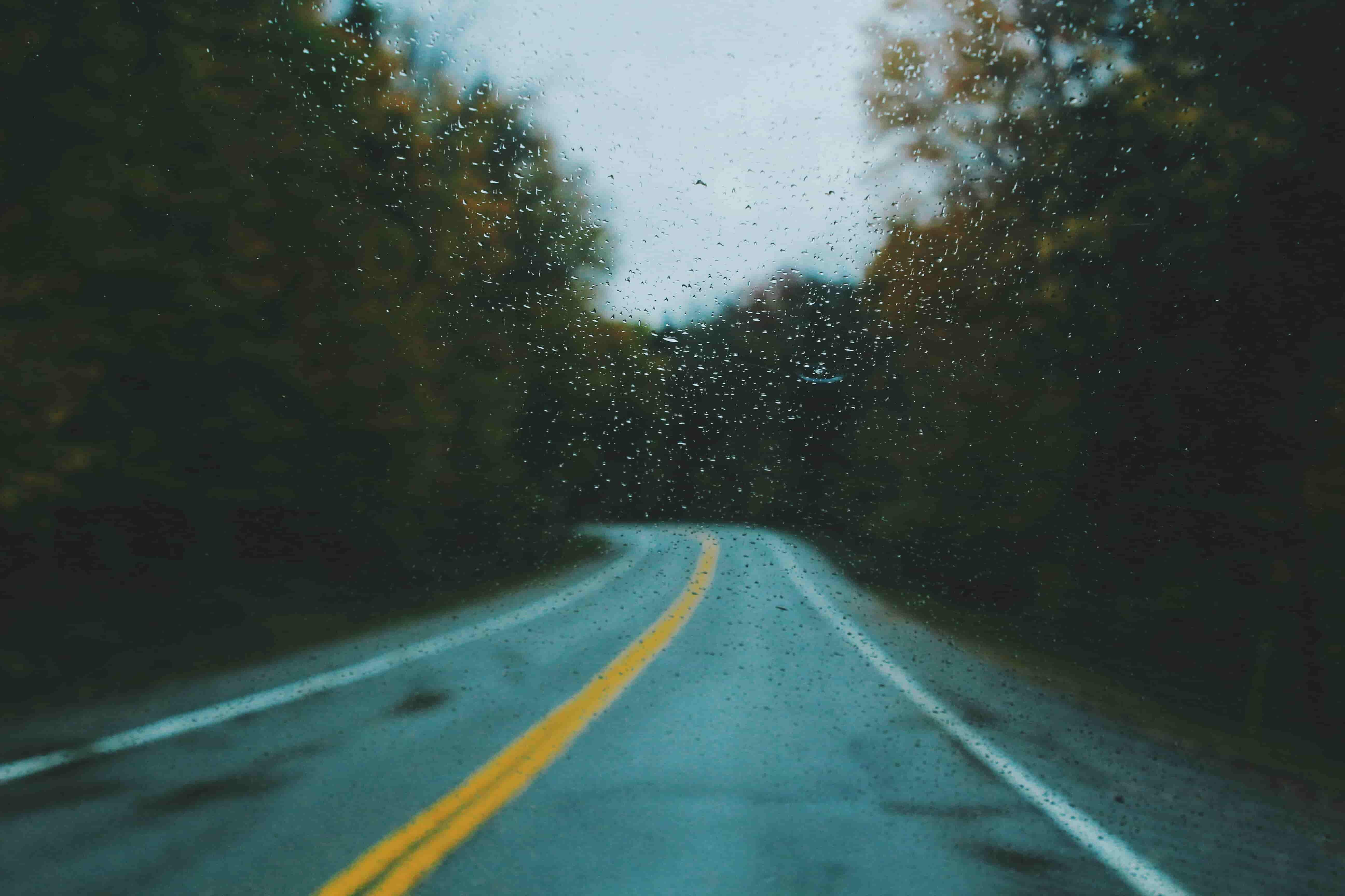 A view of a road with a yellow stripe through a raincovered windshield