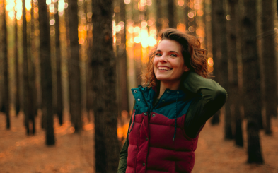 An adventurous woman standing in the woods smiling in a puffer vest